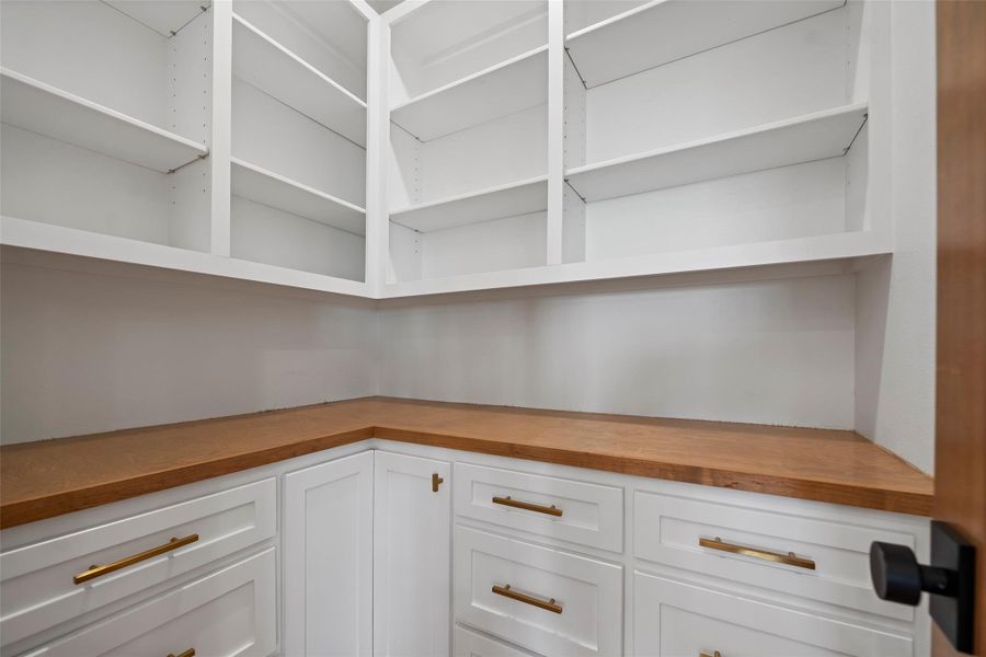 Spacious pantry with sleek white cabinetry, ample shelving, and elegant wood countertops—perfect for organized storage and easy access.
