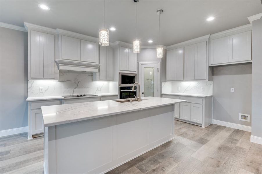 Kitchen with sink, a kitchen island with sink, hanging light fixtures, light stone counters, and black appliances