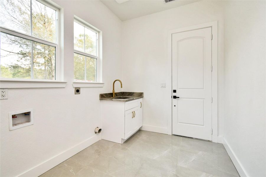 The bright utility room includes a deep soaking sink with a designer gold faucet and marble-patterned countertops.