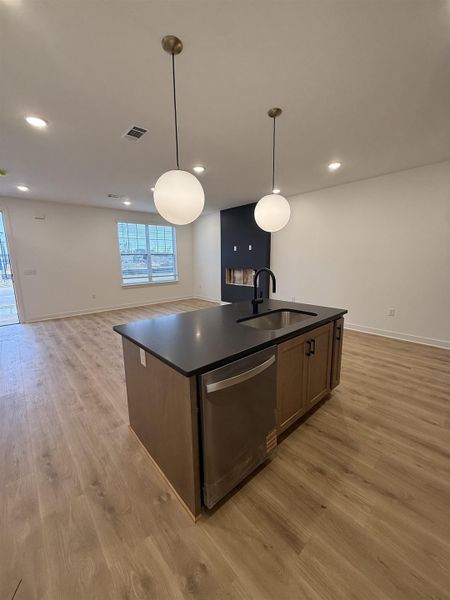 Kitchen featuring open floor plan, a center island with sink, dishwasher, pendant lighting, and light wood-style floors
