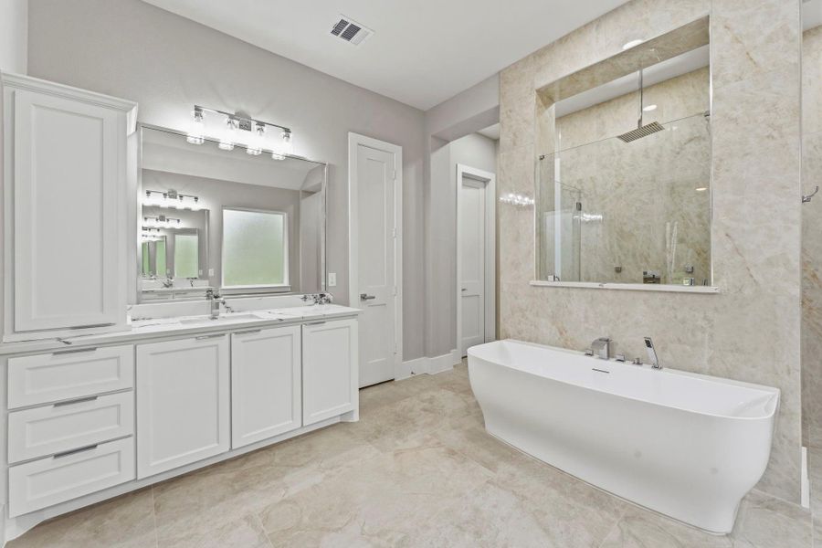 The freestanding soaking tub takes center stage against the floor to ceiling stone backdrop, creating a serene place to relax and recharge. Generous vanity storage keeps the space polished and beautifully organized.
