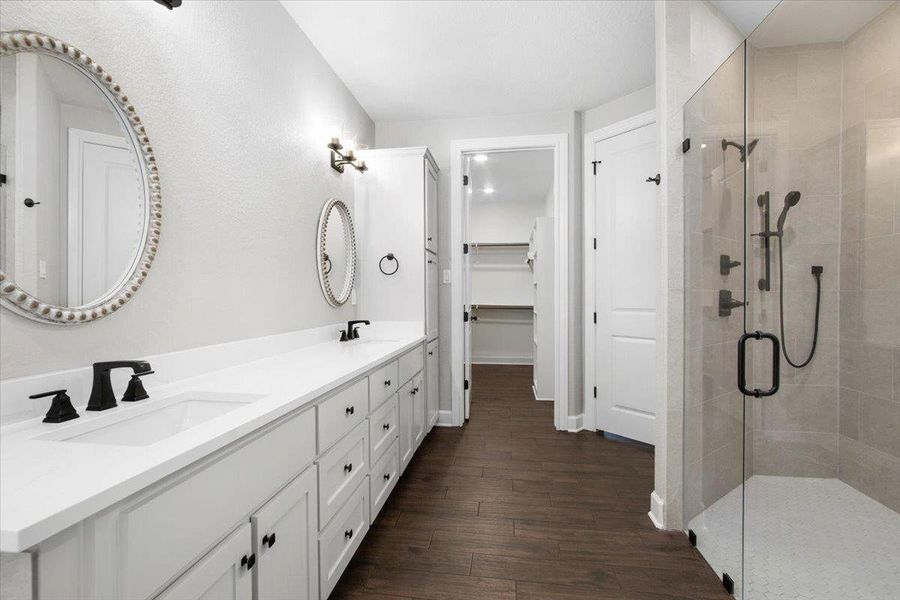 Full bath with wood finished floors, a shower stall, double vanity, and baseboards Full bath with wood finished floors, a shower stall, double vanity, and baseboards