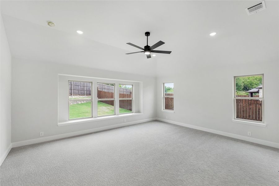 Empty bedroom with carpet flooring, ceiling fan, and multiple windows overlooking a fenced backyard Empty bedroom with carpet flooring, ceiling fan, and multiple windows overlooking a fenced backyard