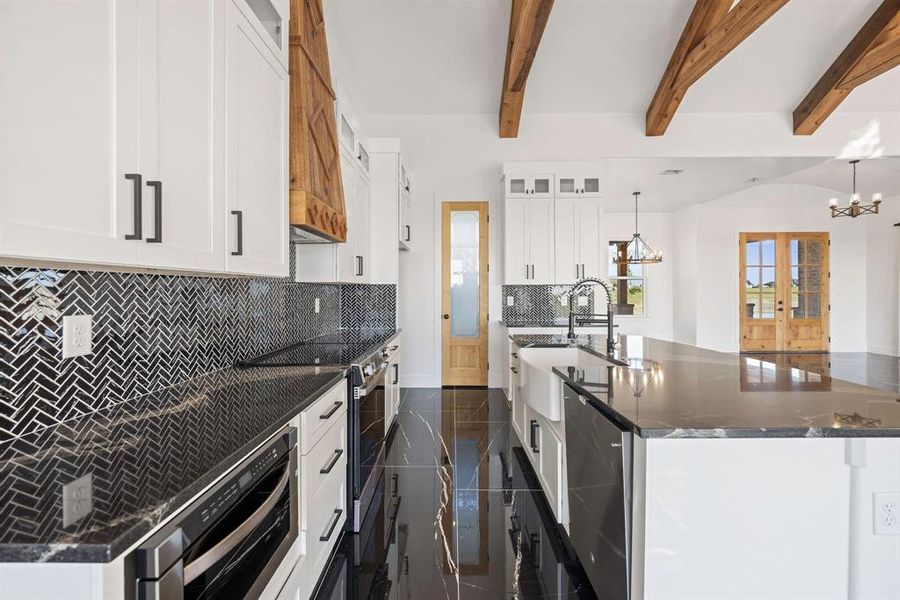 Kitchen with a chandelier, a sink, tasteful backsplash, an island with sink, and glass insert cabinets Kitchen with a chandelier, a sink, tasteful backsplash, an island with sink, and glass insert cabinets