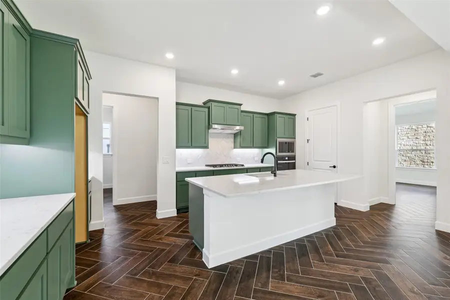 Kitchen featuring green cabinets, light stone counters, tasteful backsplash, recessed lighting, and a kitchen island with sink
