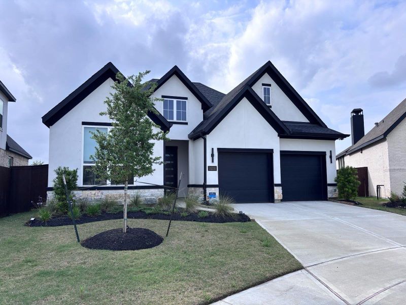 This modern home features a clean white exterior with contrasting black trim, a spacious 3-car garage, and a well-maintained front yard. The driveway is wide and welcoming, leading up to the contemporary entrance.