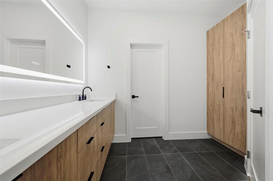 Primary Bathroom features recessed lighting. Wood vanity includes quartz countertop, dual sinks, and black fixtures. Backlit vanity mirror and black sconces enhance the space. Doorway connects directly to the separate water closet. Tile flooring extends throughout.