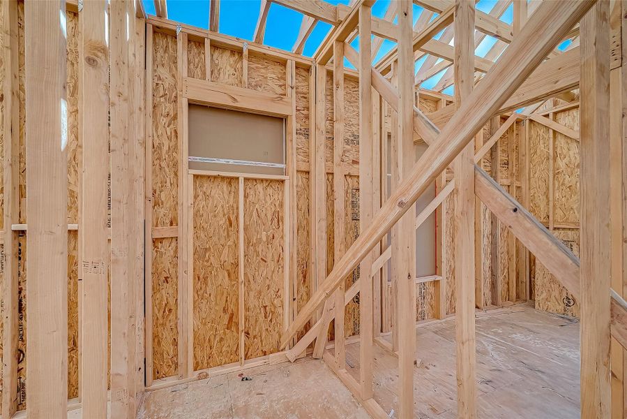 This photo shows the framing stage of new home construction, featuring exposed wooden studs and beams, with a partially completed roof structure and window opening.