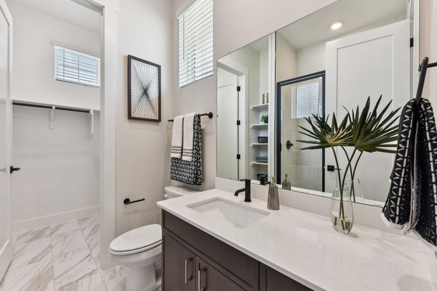 Full bathroom with vanity, a spacious closet, light marble finish flooring, and a shower with door