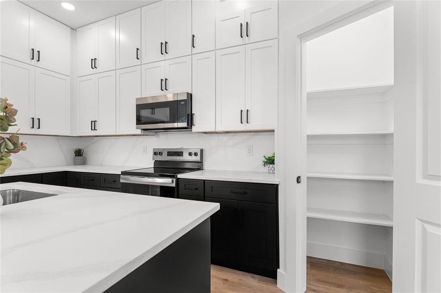 Modern kitchen featuring a stainless steel range and microwave, white upper cabinetry, contrasting black lower cabinetry, and light countertops
