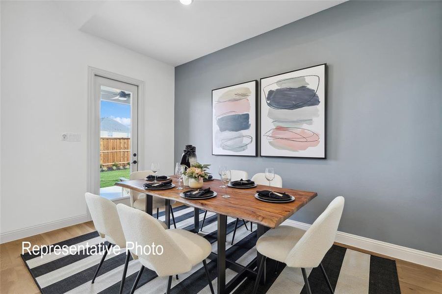 Dining area featuring wood-finish flooring, a contemporary accent wall, and a glass-paneled door leading to an outdoor space with a wooden fence
