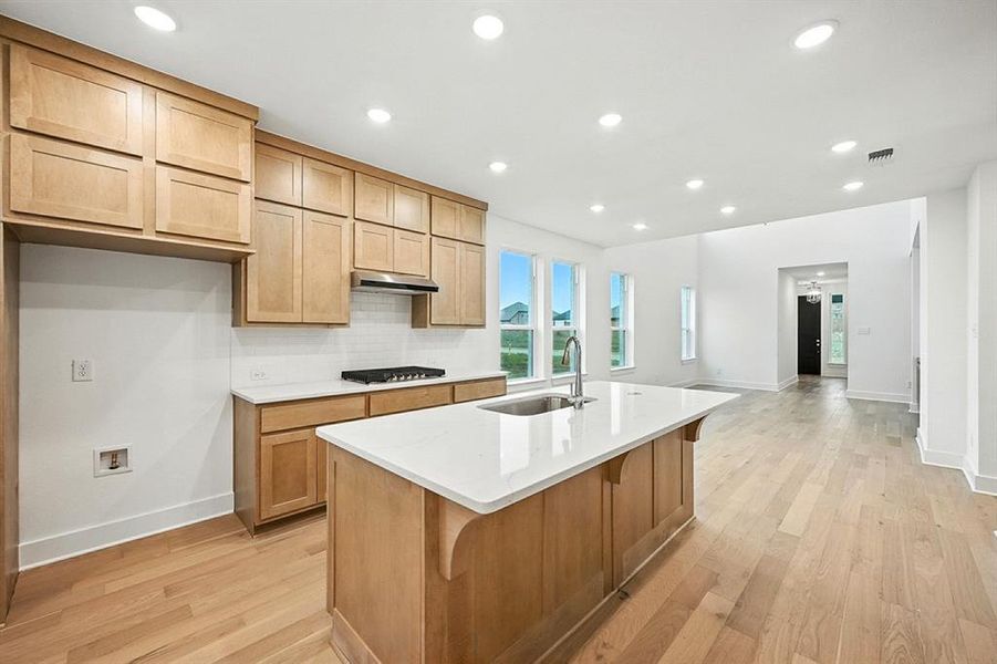Kitchen with recessed lighting, light wood-style floors, light stone countertops, decorative backsplash, and a center island with sink Kitchen with recessed lighting, light wood-style floors, light stone countertops, decorative backsplash, and a center island with sink