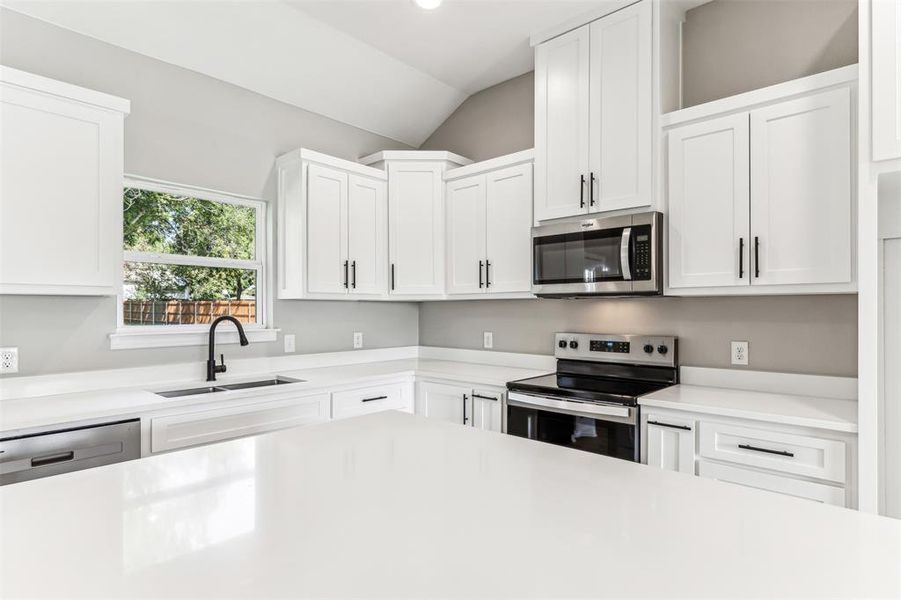 Kitchen featuring lofted ceiling, sink, appliances with stainless steel finishes, and white cabinets