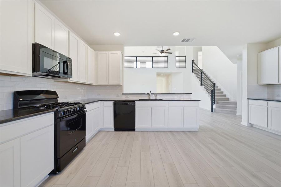 Kitchen featuring white cabinetry, dark countertops, black appliances, subway tile backsplash, and light wood-finish flooring
