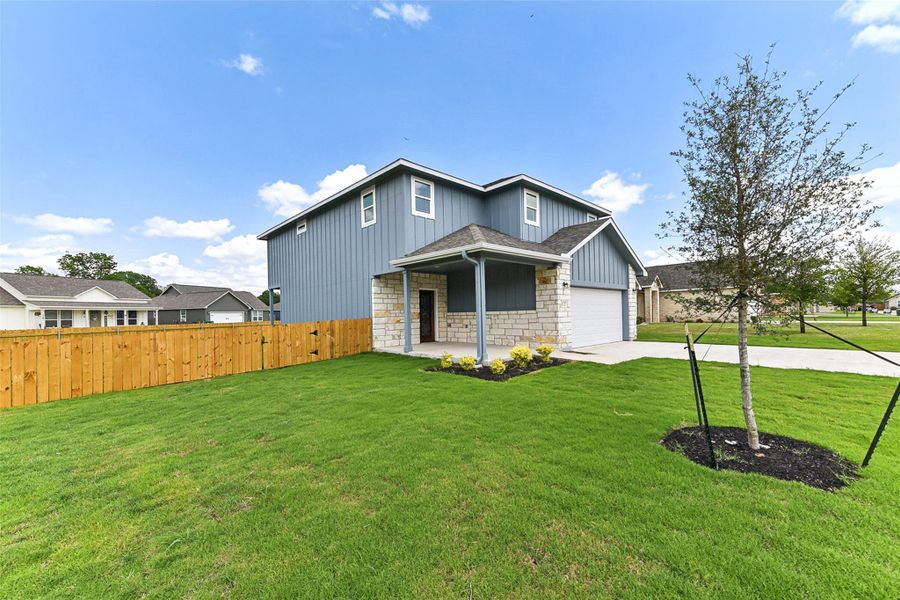 View of front facade featuring stone siding, concrete driveway, fence, board and batten siding, and a front yard View of front facade featuring stone siding, concrete driveway, fence, board and batten siding, and a front yard