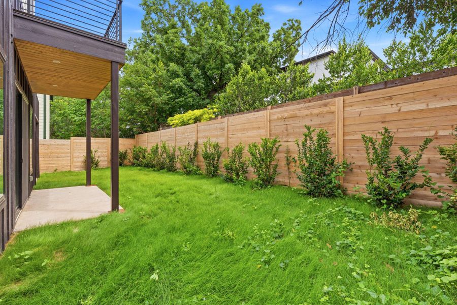 Private backyard with a horizontal slat wood fence, mature landscaping, and a concrete patio