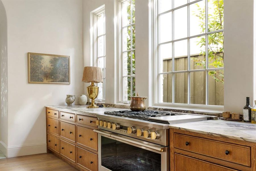Kitchen with high end stainless steel range oven, brown cabinets, healthy amount of natural light, and light wood-style floors