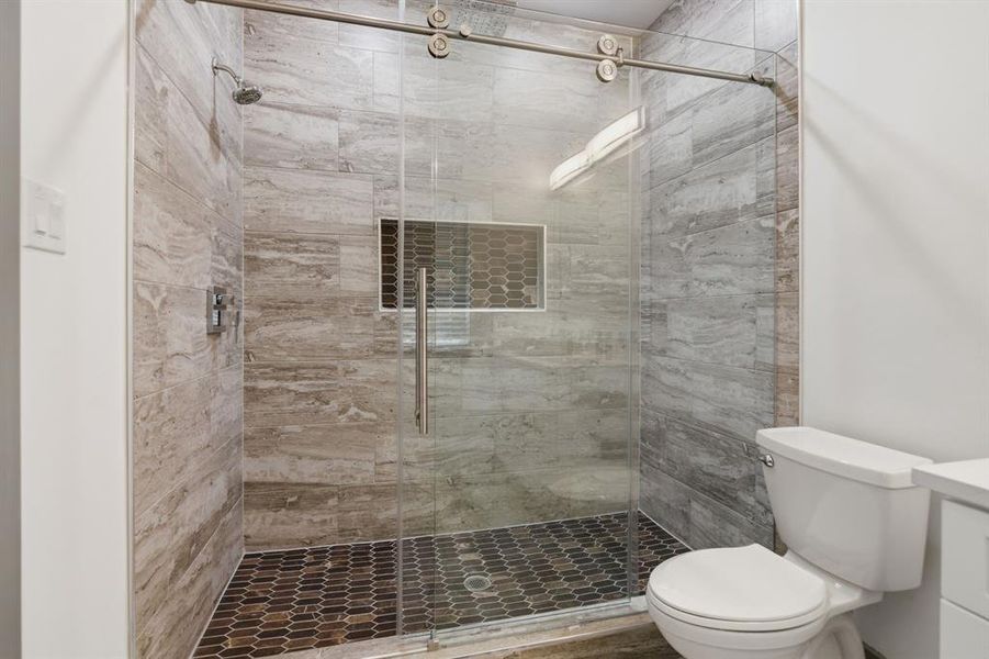 Shower enclosure with floor-to-ceiling gray tile walls, a built-in hexagonal tile niche, and a frameless glass sliding door