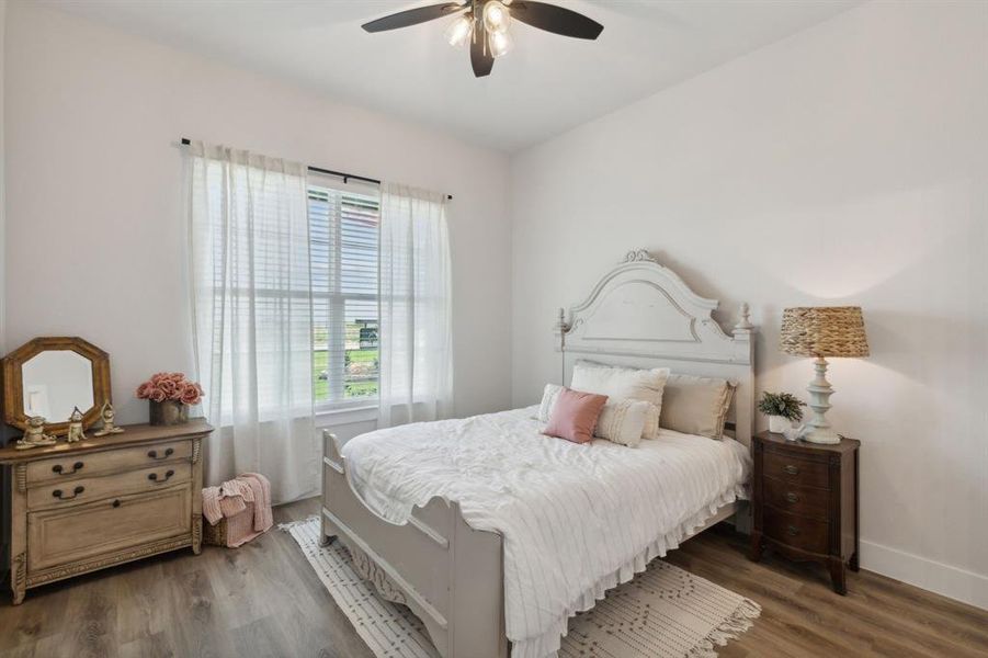Room featuring wood-finish flooring, a ceiling fan with integrated lighting, and a large window with horizontal blinds