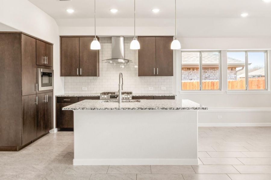 Kitchen with large granite island, dark wood cabinets, subway tile backsplash, and stainless steel range hood Kitchen with large granite island, dark wood cabinets, subway tile backsplash, and stainless steel range hood