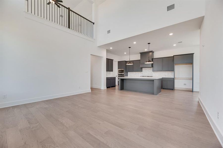 Unfurnished living room with light wood-type flooring, recessed lighting, and a high ceiling Unfurnished living room with light wood-type flooring, recessed lighting, and a high ceiling