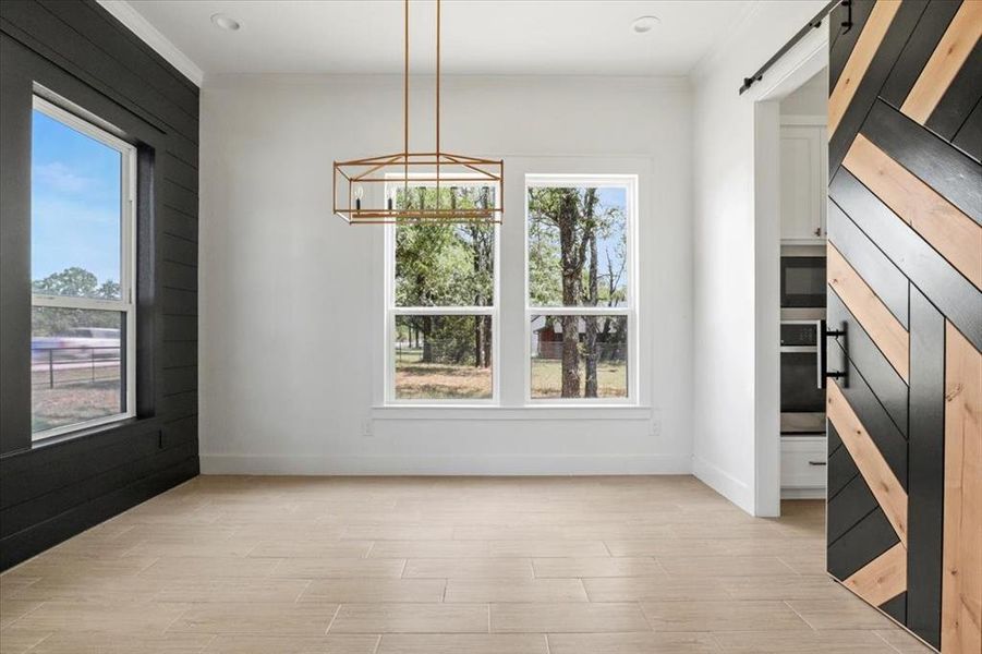 Unfurnished dining area featuring a barn door, wood tiled floors, a chandelier, and ornamental molding