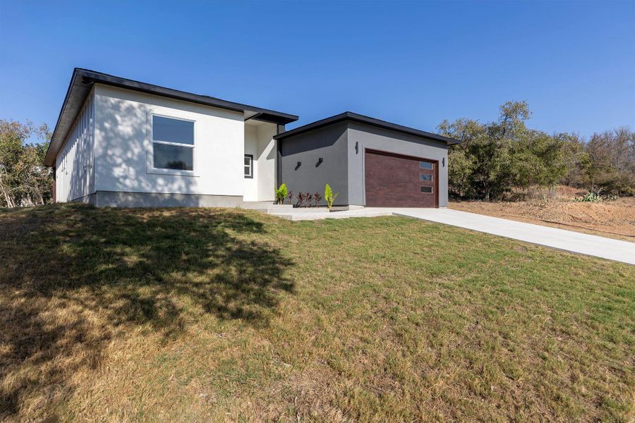 View of front of property featuring driveway, stucco siding, a front lawn, and an attached garage
