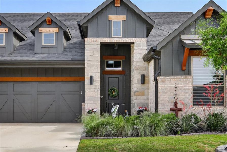Modern farmhouse-style exterior featuring a dark gray board-and-batten facade, stone accents, a dark gray shingled roof, a dark gray paneled garage door, and a concrete driveway