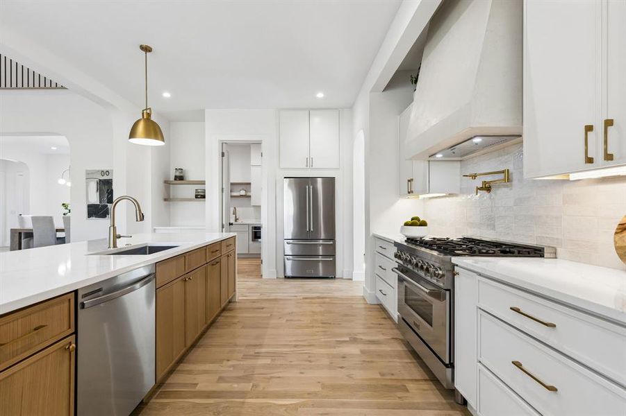 Two tone kitchen featuring arched walkways, high end appliances, pendant lighting, light wood finished floors, and light stone countertops
