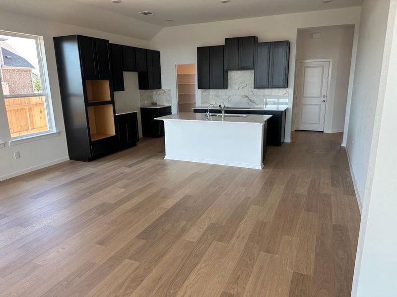 Kitchen with dark cabinetry, backsplash, a kitchen island with sink, light wood-style floors, and vaulted ceiling