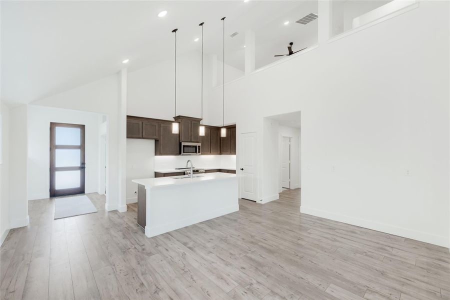 Open-concept kitchen with white island, dark wood cabinets, pendant lights, and high ceilings over light wood floors Open-concept kitchen with white island, dark wood cabinets, pendant lights, and high ceilings over light wood floors