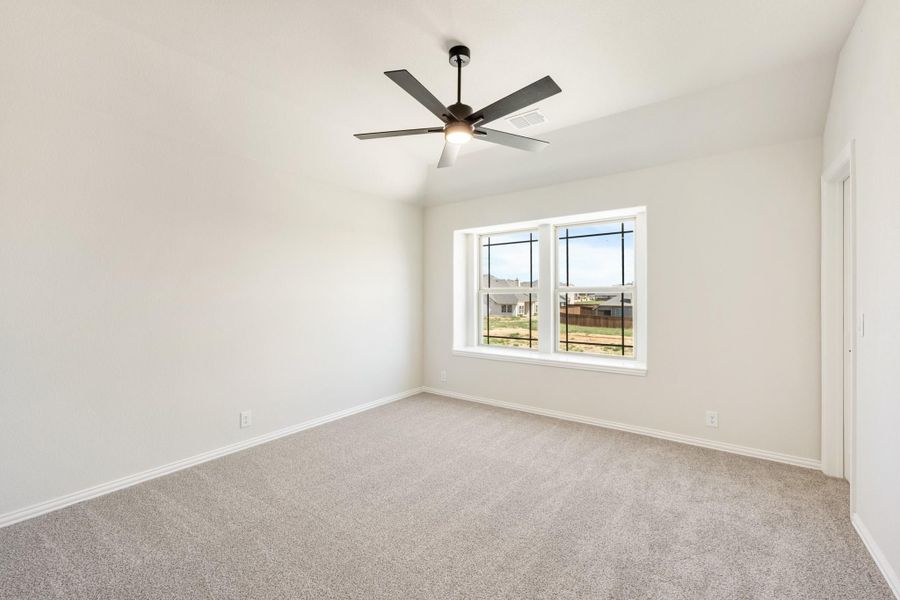 Empty bedroom with carpet flooring, ceiling fan, and a large window with backyard view
