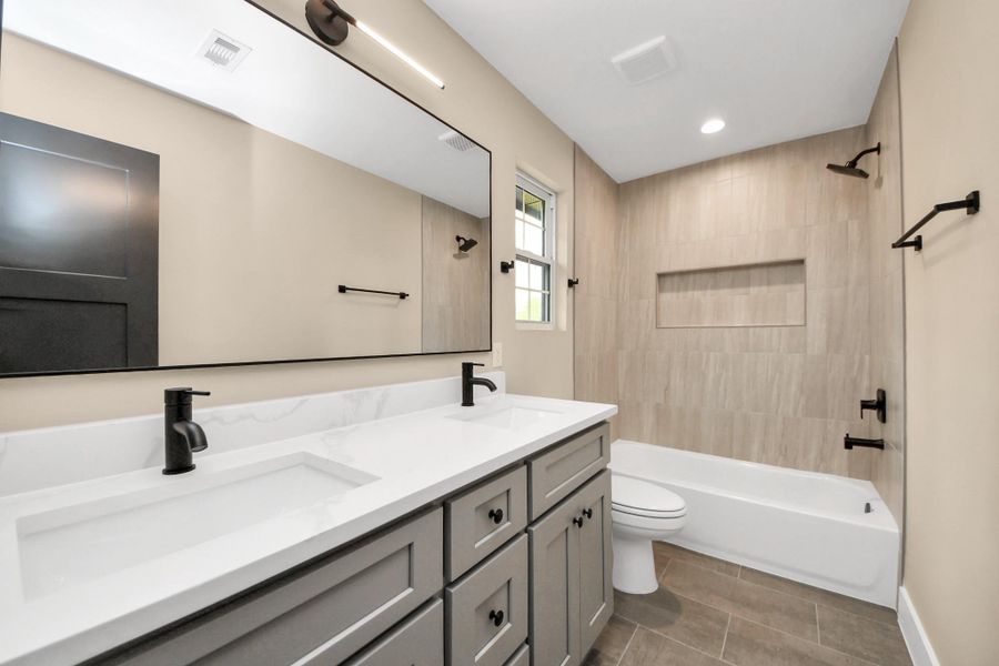 Spacious secondary bathroom featuring a double-sink vanity, modern fixtures, and a tub/shower combo with designer tile surround and built-in niche.