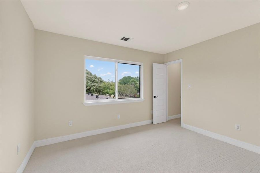 Spacious room featuring neutral carpeting, a large window, recessed lighting, and a white paneled door with dark hardware