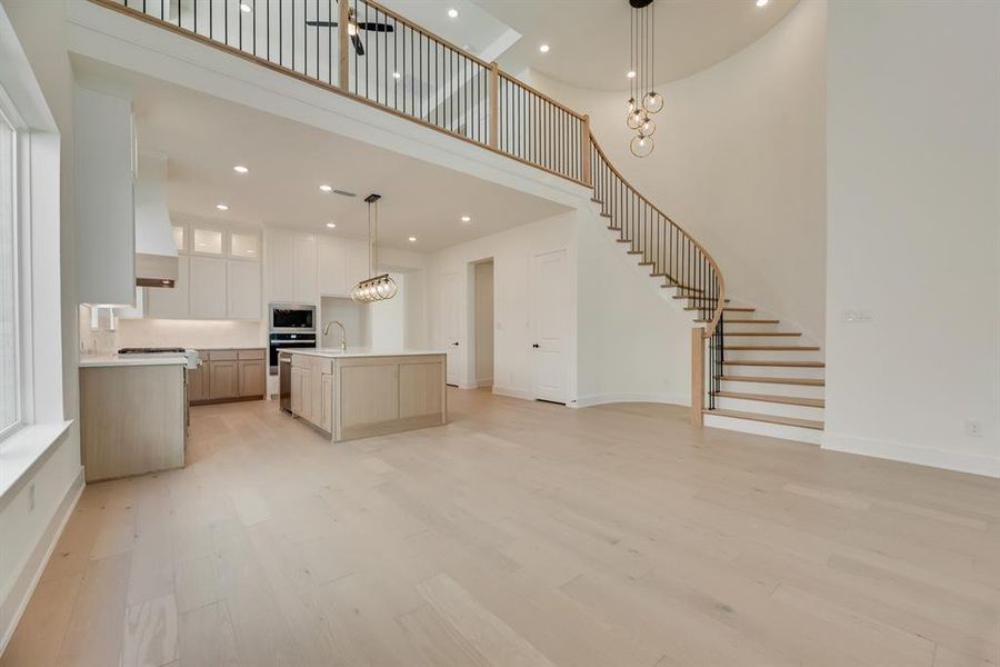 Kitchen with a towering ceiling, hanging light fixtures, glass insert cabinets, open floor plan, and an island with sink Kitchen with a towering ceiling, hanging light fixtures, glass insert cabinets, open floor plan, and an island with sink