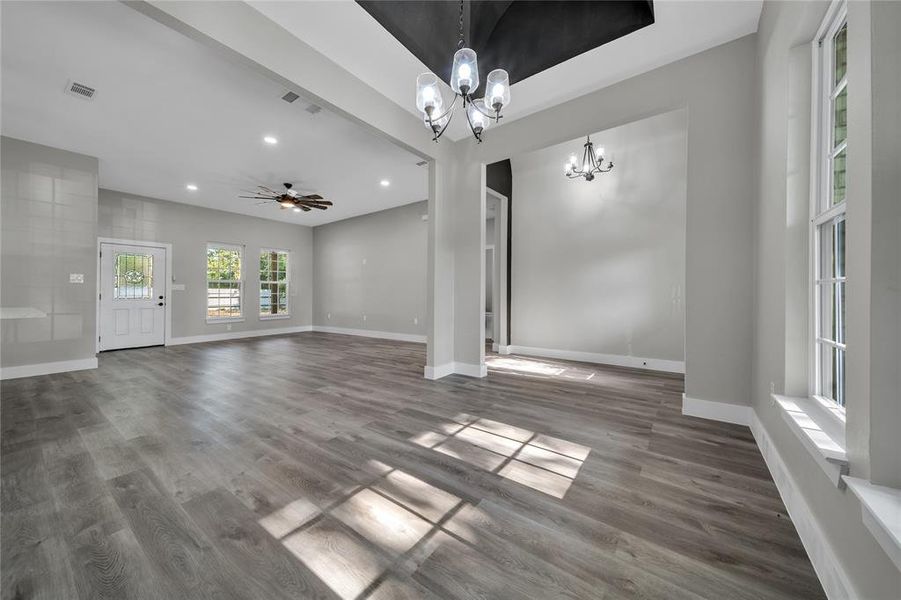 Unfurnished living room featuring ceiling fan with notable chandelier and wood-type flooring