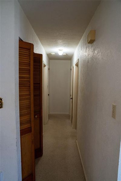 Hallway featuring a textured wall and light colored carpet