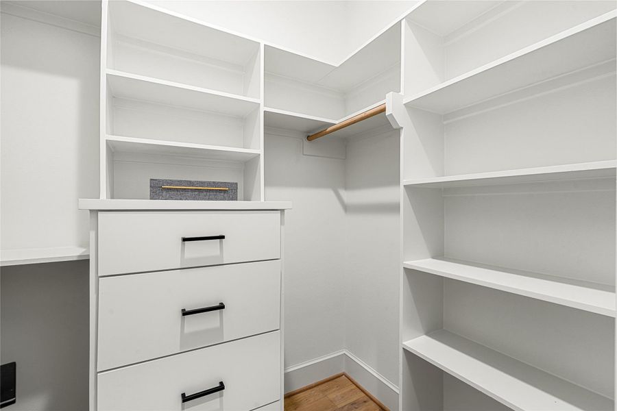 Spacious walk-in closet featuring white shelving and drawers, a spaces to hanging clothes, and ample storage on both sides. Perfect for organizing clothing and accessories.