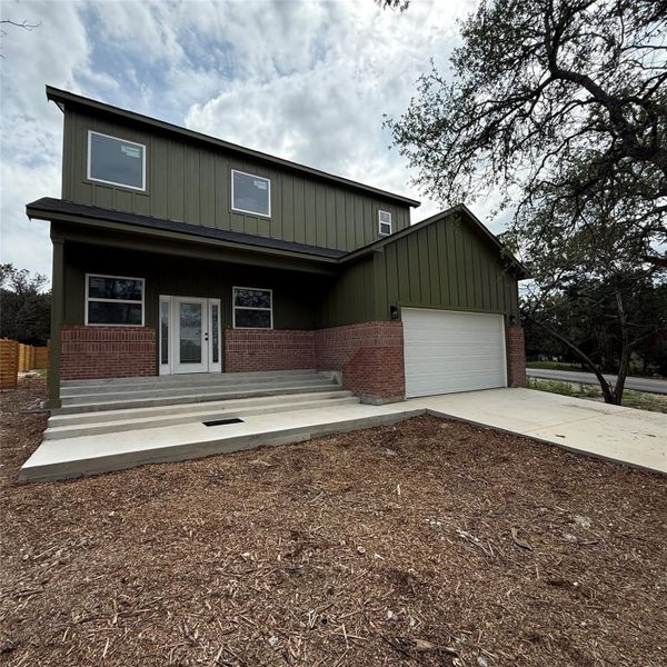 Contemporary residence featuring olive green board and batten siding, red brick accents, a two-car garage, and multiple large windows