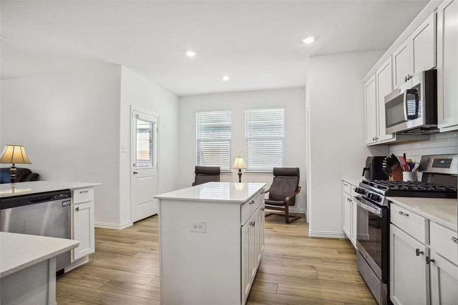 Kitchen featuring white cabinetry, a center island, light hardwood / wood-style flooring, decorative backsplash, and appliances with stainless steel finishes