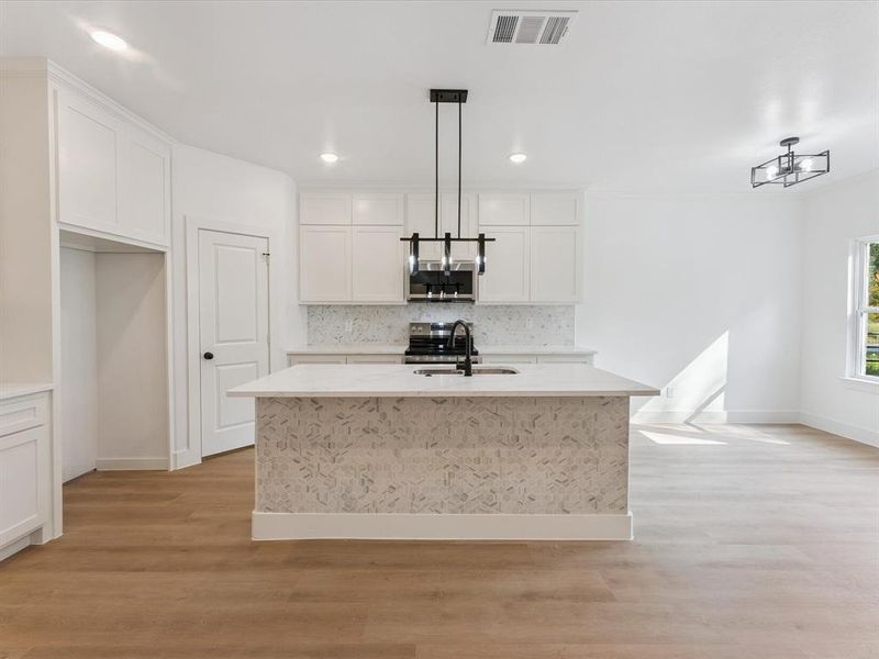 Kitchen with backsplash, light stone counters, an island with sink, light wood-style flooring, and white cabinetry