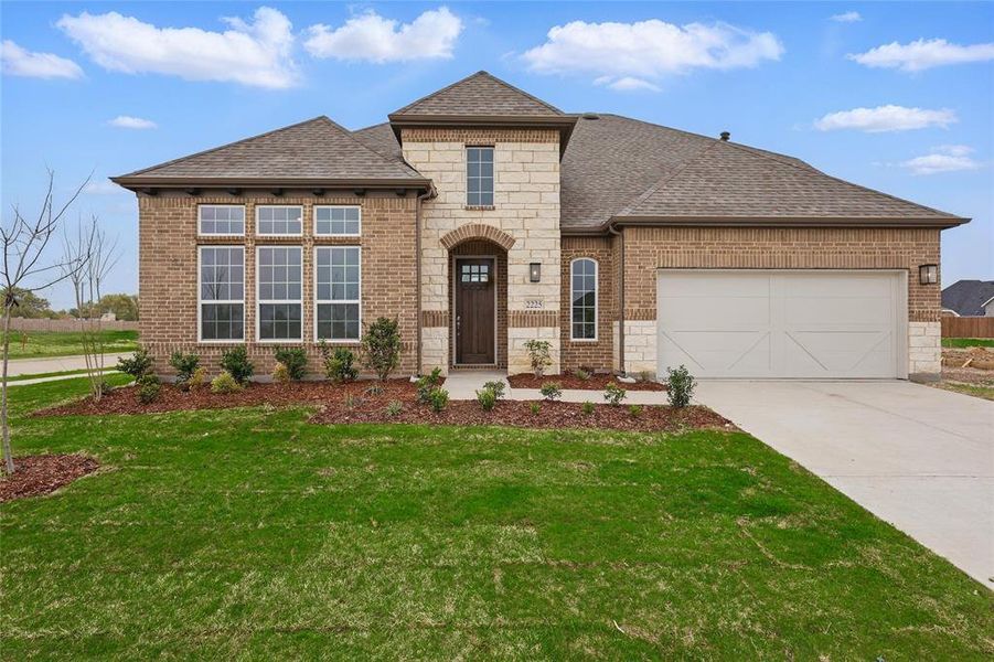 French provincial home with driveway, a front yard, brick siding, a shingled roof, and a garage