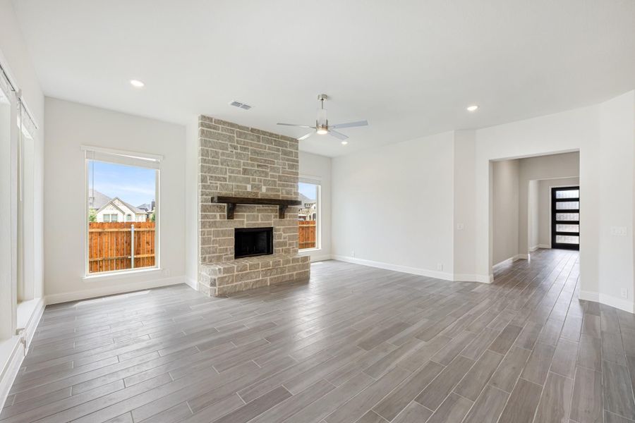 Open living room with floor-to-ceiling stone fireplace, ceiling fan, and wood-look tile floors Open living room with floor-to-ceiling stone fireplace, ceiling fan, and wood-look tile floors