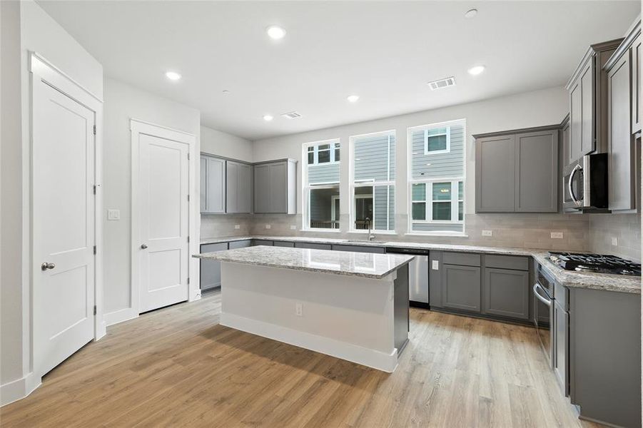 Kitchen featuring gray cabinetry, a center island, decorative backsplash, light stone countertops, and light wood-style floors
