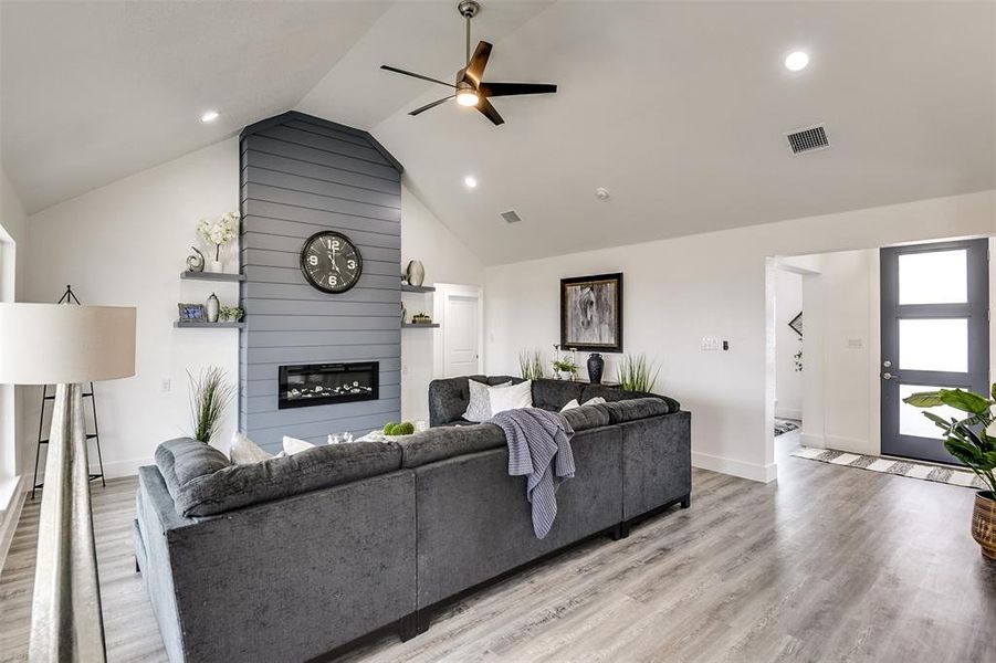 Living room with light wood finished floors, lofted ceiling, visible vents, a ceiling fan, and a large fireplace