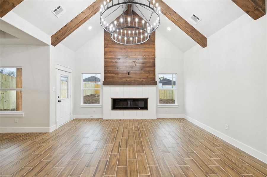 Unfurnished living room with an inviting chandelier, beam ceiling, and high vaulted ceiling