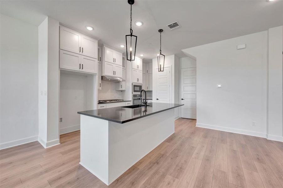 Modern kitchen featuring a dark countertop island with pendant lighting, white cabinetry, a built-in oven, and wood-finish flooring Modern kitchen featuring a dark countertop island with pendant lighting, white cabinetry, a built-in oven, and wood-finish flooring