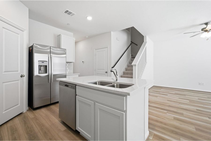 Kitchen with stainless steel appliances, a center island with sink, white cabinetry, and light wood finished floors Kitchen with stainless steel appliances, a center island with sink, white cabinetry, and light wood finished floors
