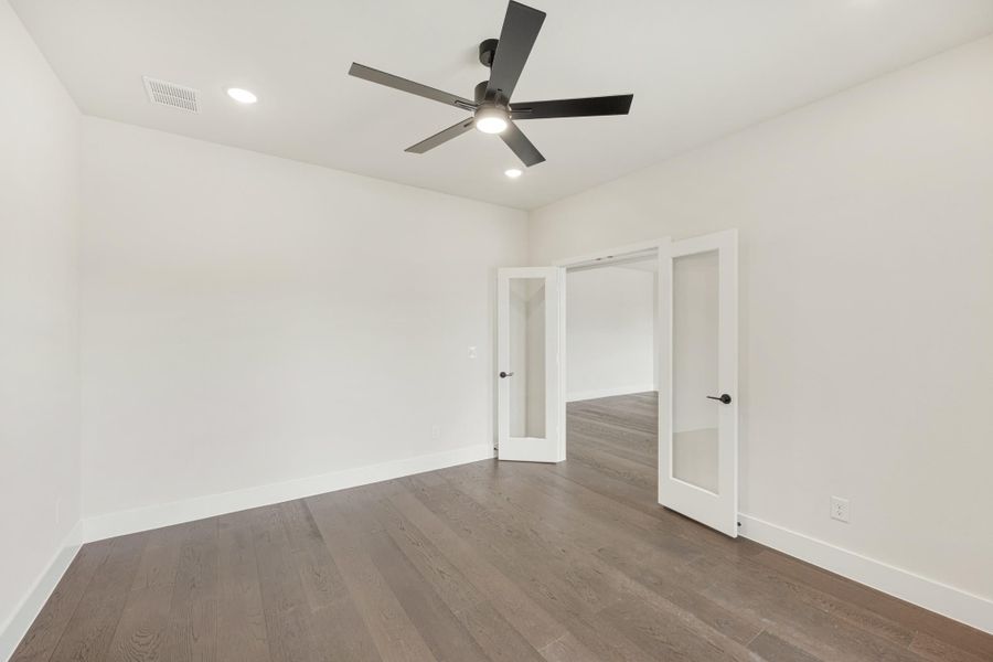 Empty room with dark hardwood floors, black ceiling fan, and French doors with glass panels