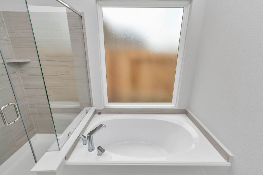The primary en-suite has a soaking tub to give you that spa experience. The large privacy window allow lots of nature light in the space. Sample photo of completed home with similar floor plan. Actual colors and selections may vary.